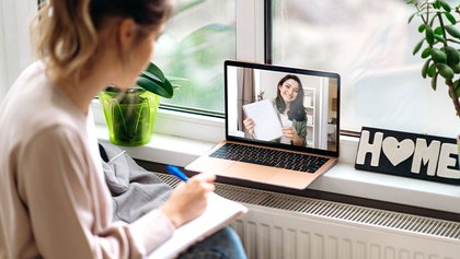 Mujer tomando apuntes mientras participa en una reunión online.