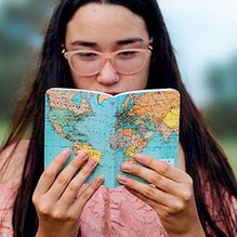 Chica de pelo moreno y gafas, leyendo un mapa del mundo al aire libre