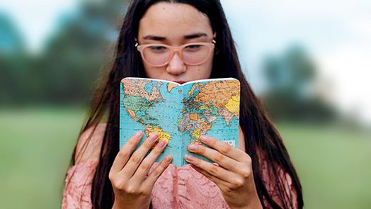 Chica de pelo moreno y gafas, leyendo un mapa del mundo al aire libre